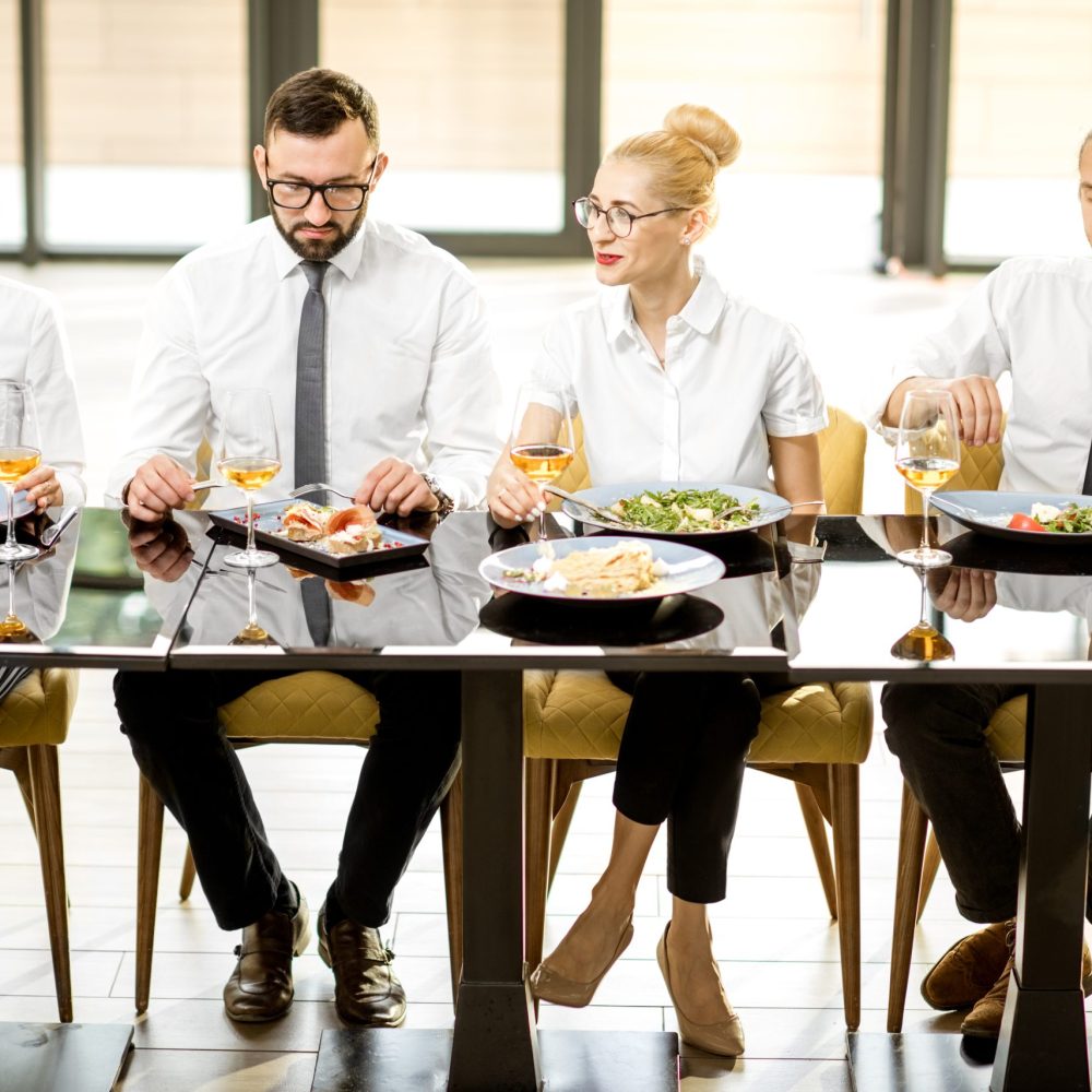 Business people dressed in white shirts having business lunch sitting in a row at the table in the modern restaurant
