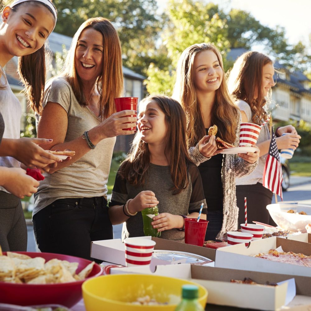 Girls stand talking at a block party food table, close up